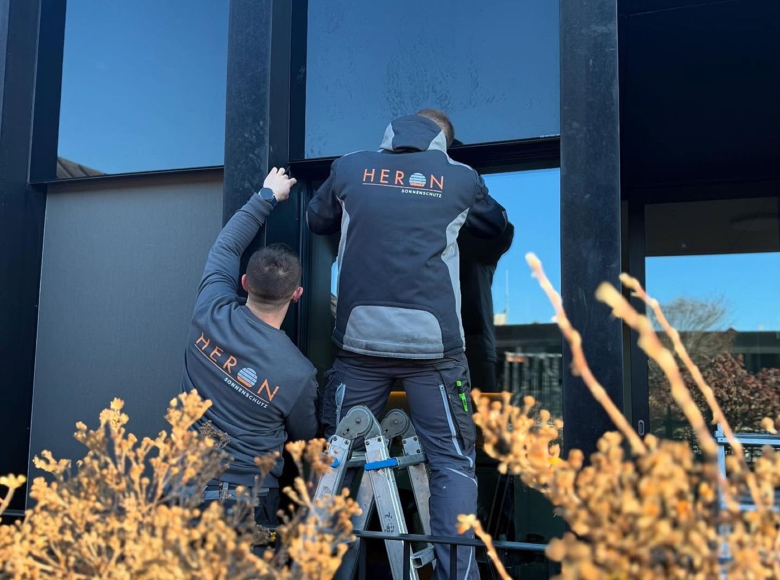 Zwei Heron Sonnenschutz Mitarbeiter bei der Montage an einer Fensterfront